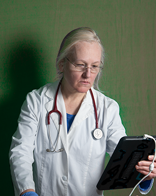 Doctor using ultrasound imaging to diagnose a child's injury. Photograph of the doctor wearing a lab coat and stethoscope and holding a tablet. 
